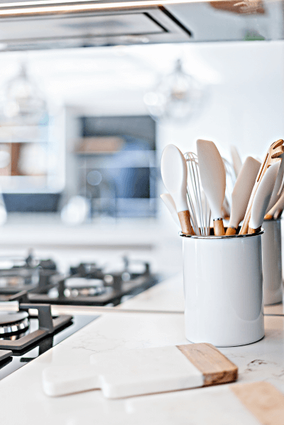 Modern kitchen with white utensils in a jar next to a sleek gas stove and cutting board.