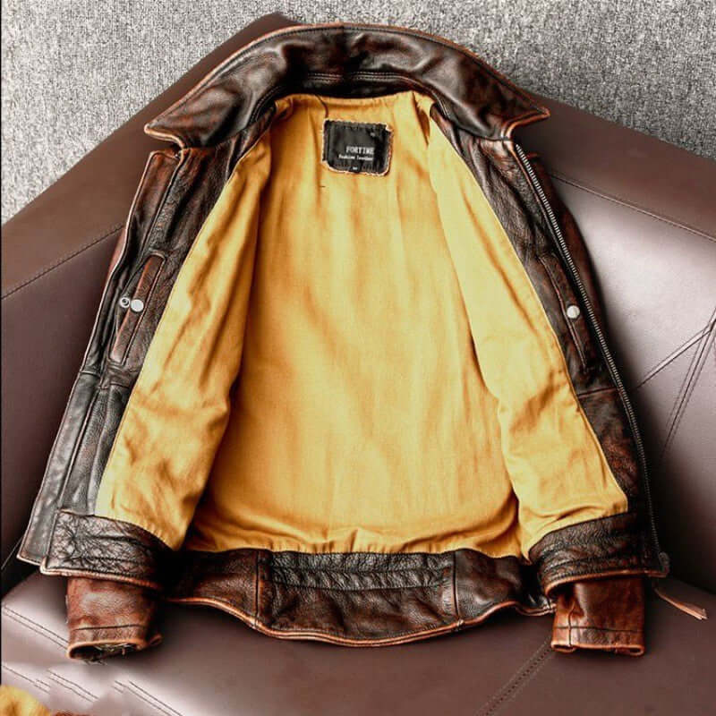 Men's vintage distressed brown cowhide leather jacket with yellow lining, fashion minimalist style, shown open on leather chair.